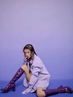 a woman sitting on the ground with her legs crossed wearing purple boots and a flower in her hair