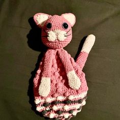 a crocheted pink and white cat sitting on top of a bed