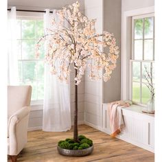 a white tree with pink flowers in a living room next to a chair and window