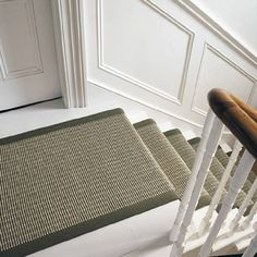 the stairs are made of wood and have green rugs on each step, along with white painted walls