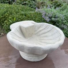 a white bowl sitting on top of a table in front of some bushes and flowers