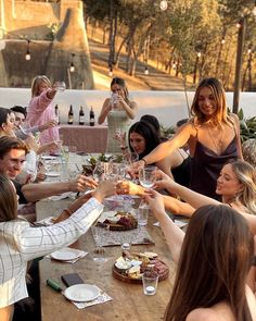 a group of people sitting around a wooden table with wine glasses in their hands and plates on the table