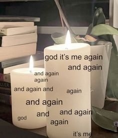 two candles with the words god it's me again and again on them sitting next to some books