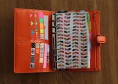 an orange binder is open on top of a wooden table with papers and pens