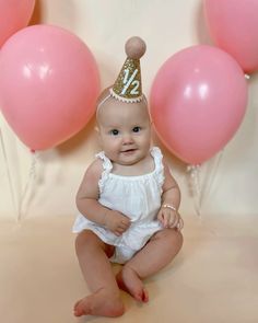 a baby wearing a birthday hat sitting in front of balloons