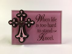 a pink plaque with a black and white cross on it that says, when life is too hard to stand kneel