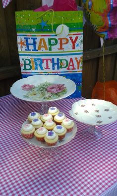 a table topped with lots of cupcakes next to a sign and cake plate