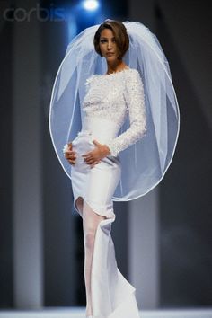 a woman in a white wedding dress and veil on the runway at a fashion show