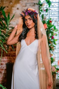 a woman in a white dress and veil with flowers on her head is posing for the camera