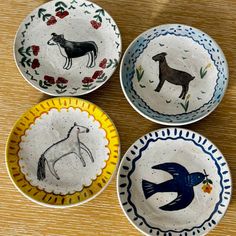 four hand painted bowls with horses and birds in them on a wooden table top next to each other