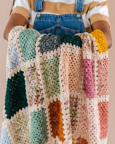 a crocheted blanket is being held by a person wearing overalls and suspenders