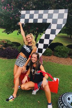 two women posing for the camera in front of a checkered number