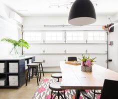 a room with a table, chairs and plants on the floor in front of a white wall