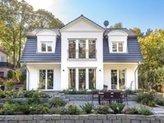 a large white house with lots of windows and plants in the front yard, surrounded by greenery