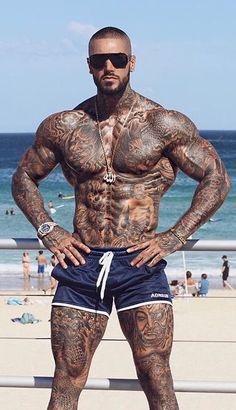 a man with tattoos standing on the beach