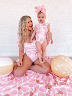 a woman holding a baby sitting on top of a pink and white polka dot blanket