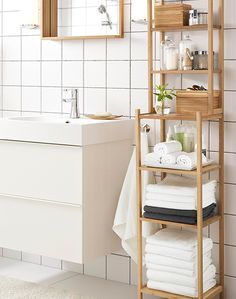 a bathroom with white tiled walls and flooring, including a wooden shelf that holds towels