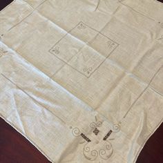 a table cloth with embroidered designs on it sitting on top of a wooden table next to a pair of scissors