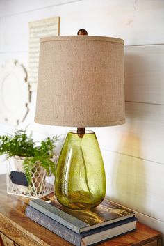 a green glass lamp sitting on top of a wooden table next to a stack of books