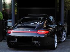 a black porsche sports car parked in front of a building with its doors open and windows closed