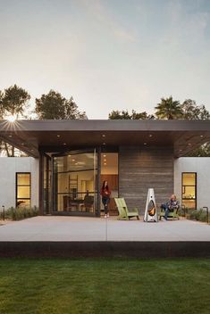 two people sitting on lawn chairs in front of a modern house with glass doors and windows