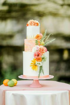 a three tiered cake with flowers and greenery sits on a pink tablecloth