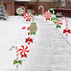 candy canes are lined up in the snow near a brick house with red and green bows on them