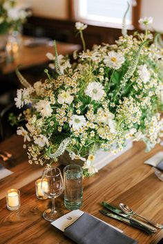 a vase filled with white flowers sitting on top of a wooden table next to candles