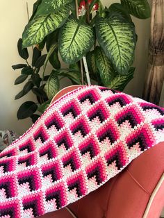 a pink and black crocheted blanket sitting on top of a chair next to a potted plant