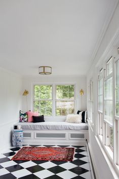 a black and white checkered floor in a room with a window, rug and bed