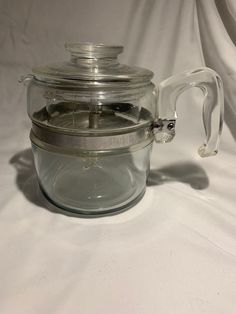 a glass teapot with a lid and handle on a white tablecloth covered background