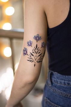 a woman with a tattoo on her arm and purple flowers in the middle of her arm