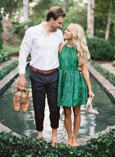 a man and woman standing next to each other in front of a pond with green plants