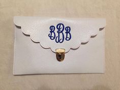 a white leather wallet with blue monogrammed letters on the front and an angel wing