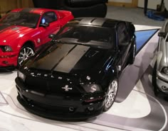 three toy cars are on display in a showroom, one is black and the other is red