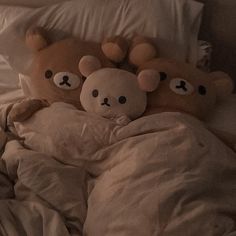 two teddy bears are laying in bed under the covers