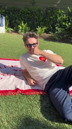 a man laying on top of a red and white blanket next to a green field