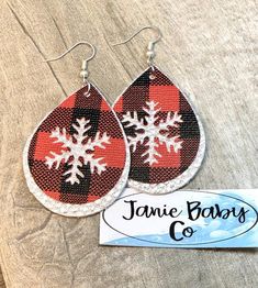 the red and black plaid snowflake earrings are next to a sign that says, jamie