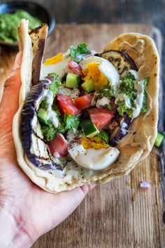 a hand holding a pita filled with vegetables