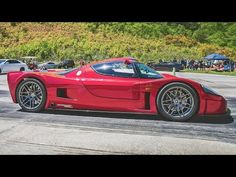 a red sports car driving down a street next to other cars and people in the background