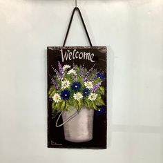 a welcome sign hanging on a wall with flowers in a bucket and the words welcome