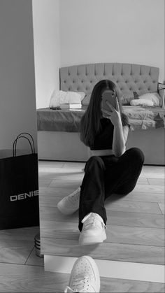 a woman sitting on the floor while looking at her cell phone and taking a selfie