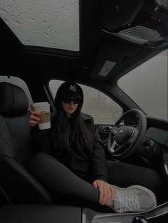 a woman sitting in the driver's seat of a car holding a coffee cup