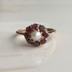 A vintage 9 carat gold Garnet and Pearl cluster ring.  CONDITION: Wear consistent with age and use. Please see photos for more detail. Stones all in good condition. HALLMARKED 9 CARAT GOLD, ASSAYED IN LONDON 1957 SETTING DIAMETER: 10mm  GARNET SIZE: 3mm (0.10 carats) PEARL SIZE: 4mm (0.33 carats) BAND WIDTH NARROWEST: 1.5mm RING SIZE: UK: J | US: 4 3/4 WEIGHT: 2.3 grams (SZ) 50s Wedding Ring, Garnet And Pearl Ring, Vintage Yellow Gold Pearl Ring With Gemstone, Vintage 14k Stamped Cluster Rings, Vintage Gold Cluster Ring With Gemstones, Vintage White Pearl Ring, Vintage White Cluster Ring With Gemstone, Vintage Cluster Rings For Gifts, Vintage Cluster Rings As Gift