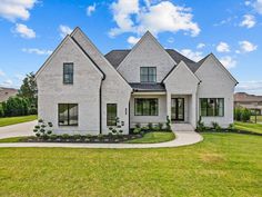 a large white brick house in the middle of a grassy area with trees and bushes