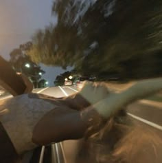 a person riding in the back of a car on a road at night with trees and street lights