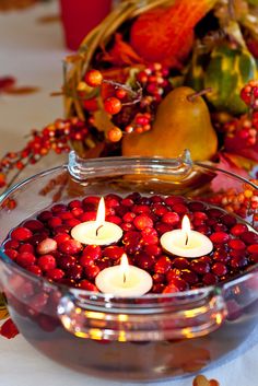 candles in a bowl filled with cranberries and pomegranates on a table