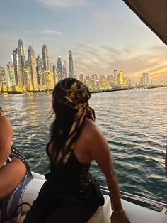 two women sitting on the back of a boat in front of a cityscape