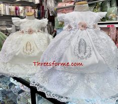 two white dresses are on display in a store window, one is wearing a tiara and the other has a dress made from lace