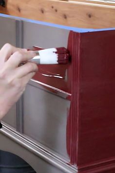 a person painting the side of a cabinet with red paint